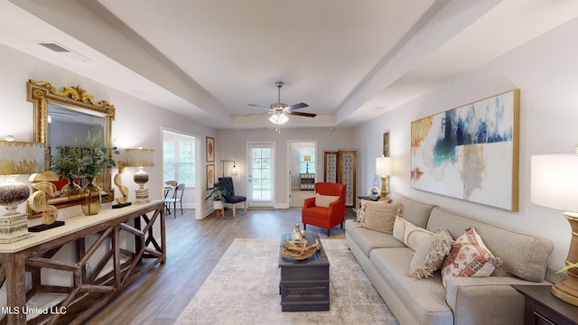 living room featuring ceiling fan, wood-type flooring, and a tray ceiling