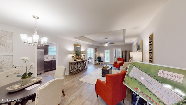 living room with ceiling fan with notable chandelier, light wood-type flooring, a tray ceiling, and plenty of natural light