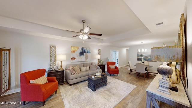 living room featuring ceiling fan with notable chandelier, light wood-type flooring, and a raised ceiling