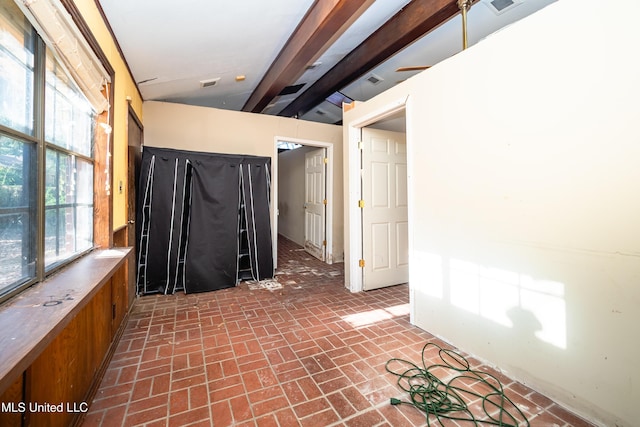 spare room featuring brick floor, visible vents, and beamed ceiling