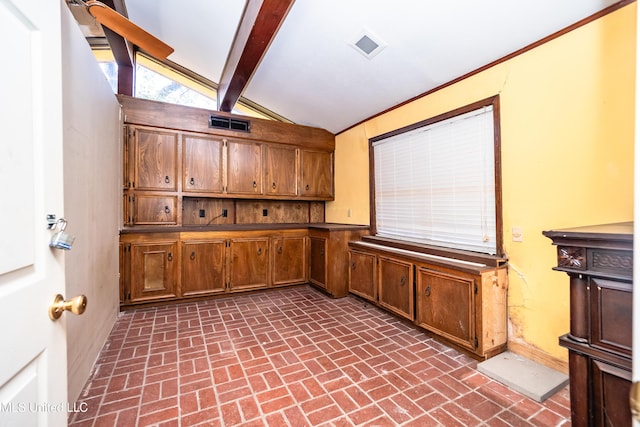 kitchen with lofted ceiling with beams, brown cabinetry, and brick floor