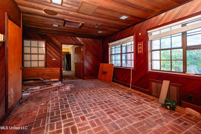 unfurnished room with plenty of natural light, wooden ceiling, and wooden walls