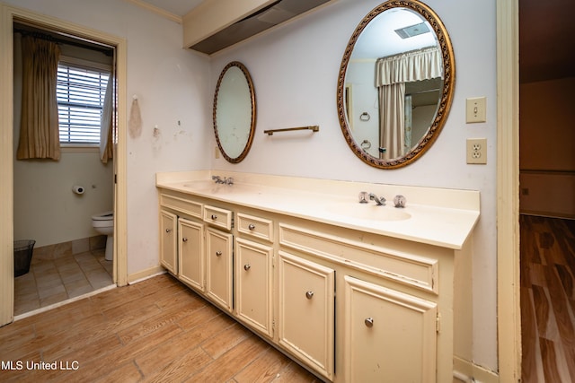 full bath featuring toilet, wood finished floors, a sink, baseboards, and double vanity