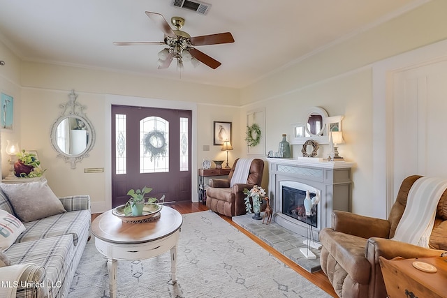 living room featuring ceiling fan, crown molding, a fireplace, and light wood-type flooring