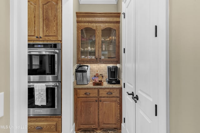 705 Brookwood Cir, Brandon, MS 39042 - kitchen with stainless steel double oven, backsplash, glass insert cabinets, brown cabinets, and light countertops