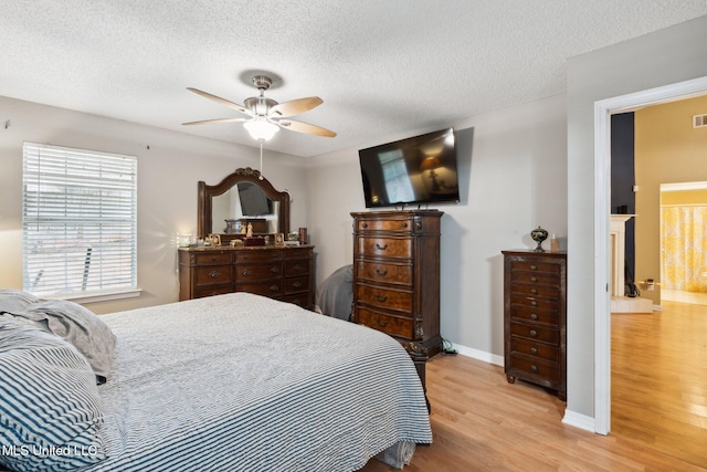 bedroom featuring ceiling fan, light wood-type flooring, a textured ceiling, and ensuite bath