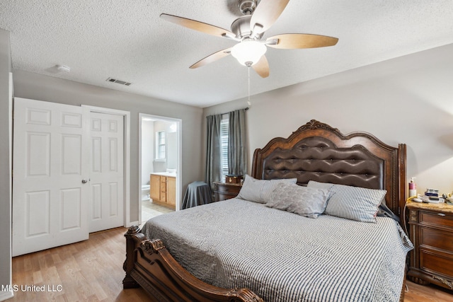 bedroom with a textured ceiling, light wood-type flooring, ceiling fan, and connected bathroom