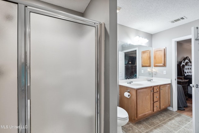 bathroom with a shower with door, vanity, a textured ceiling, and toilet