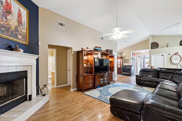 living room with ceiling fan, light wood-type flooring, a fireplace, and vaulted ceiling