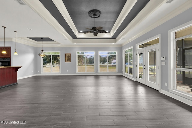 unfurnished living room with dark wood-type flooring, a tray ceiling, crown molding, baseboards, and ceiling fan