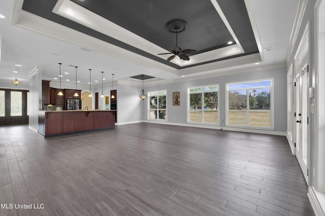 unfurnished living room with a tray ceiling, a healthy amount of sunlight, ceiling fan, and dark wood-style flooring