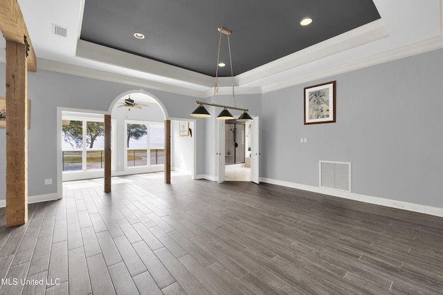 unfurnished dining area featuring a raised ceiling, dark wood-style floors, arched walkways, and visible vents