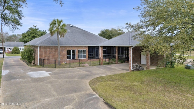 ranch-style house featuring brick siding, roof with shingles, a front lawn, and fence