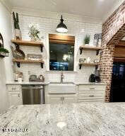 bar featuring light stone countertops, brick wall, sink, dishwasher, and white cabinets