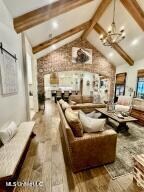 living room with hardwood / wood-style floors, vaulted ceiling with beams, a barn door, and a notable chandelier