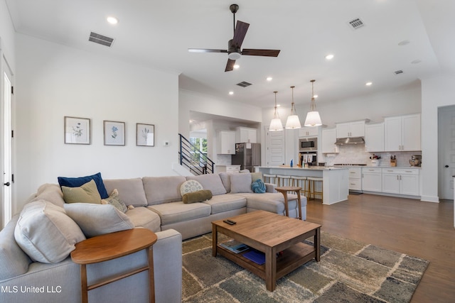 living area with dark wood finished floors, visible vents, and crown molding