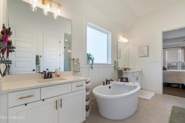 bathroom with two vanities, a freestanding bath, a sink, vaulted ceiling, and connected bathroom