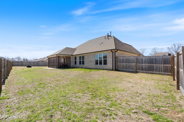 rear view of house featuring a lawn, a fenced backyard, roof with shingles, a sunroom, and brick siding