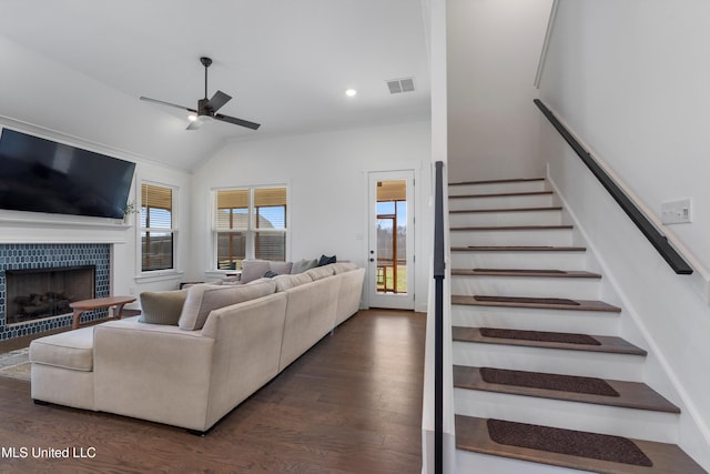 living room featuring visible vents, a ceiling fan, a tiled fireplace, dark wood finished floors, and stairway