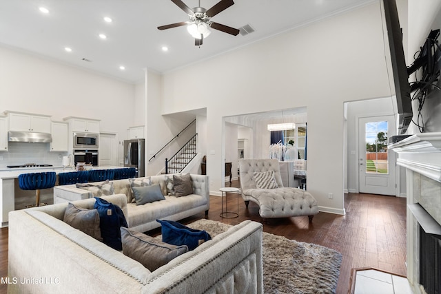 living room featuring dark wood-type flooring, crown molding, a high ceiling, and ceiling fan