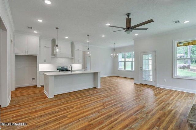 kitchen featuring light hardwood / wood-style floors, ceiling fan with notable chandelier, a center island with sink, and white cabinetry