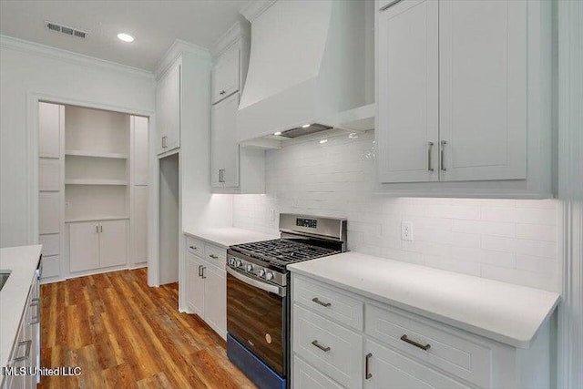 kitchen featuring light hardwood / wood-style flooring, stainless steel range with gas stovetop, custom exhaust hood, and white cabinets