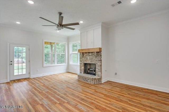 unfurnished living room featuring ornamental molding, light wood-type flooring, a textured ceiling, a brick fireplace, and ceiling fan