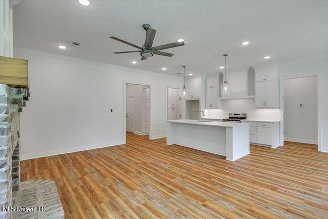 kitchen with custom range hood, stainless steel stove, a center island with sink, and light hardwood / wood-style flooring