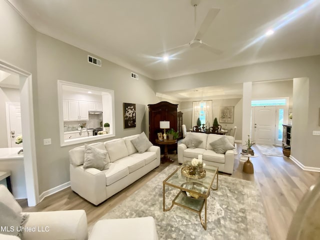living area with light wood-style floors, a ceiling fan, baseboards, and a chandelier