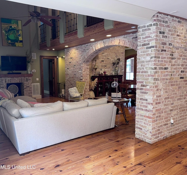 236 Sawbridge Dr, Ridgeland, MS 39157 - living room featuring a fireplace, ceiling fan, brick wall, wood finished floors, and arched walkways