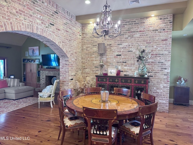 236 Sawbridge Dr, Ridgeland, MS 39157 - dining room with a brick fireplace, hardwood / wood-style floors, a chandelier, brick wall, and arched walkways