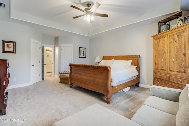 bedroom with a tray ceiling, light colored carpet, visible vents, and baseboards