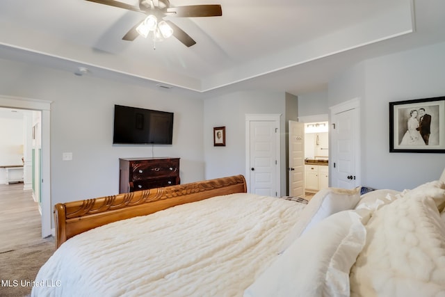 bedroom with a ceiling fan, a raised ceiling, light colored carpet, and connected bathroom