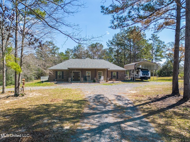 view of front of property featuring a front lawn, covered porch, gravel driveway, a detached carport, and brick siding