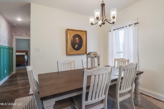 dining space featuring dark wood-type flooring, an inviting chandelier, wainscoting, wallpapered walls, and baseboards