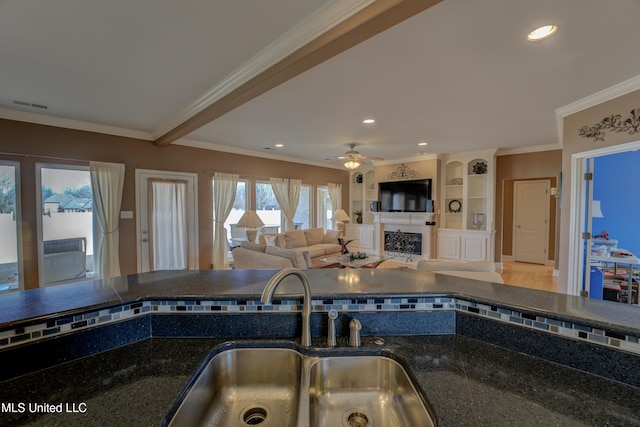 kitchen with ceiling fan, ornamental molding, sink, and dark stone counters