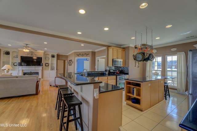 kitchen with ceiling fan, stainless steel appliances, a kitchen island, a kitchen breakfast bar, and light tile patterned flooring