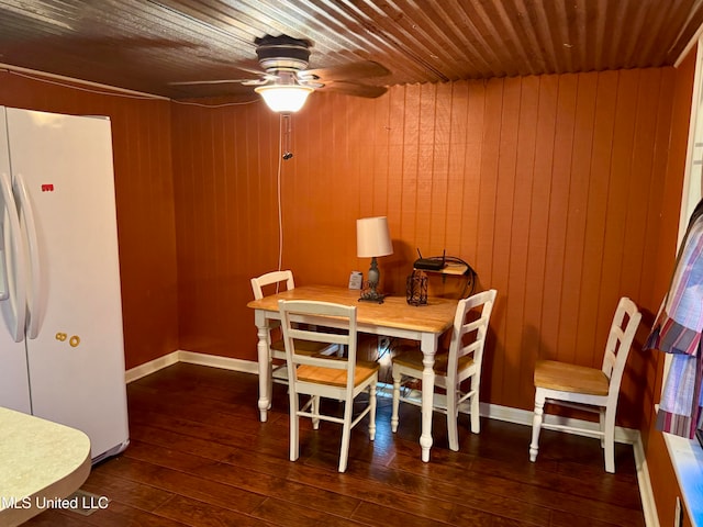 dining space with dark hardwood / wood-style flooring, ceiling fan, and wooden walls