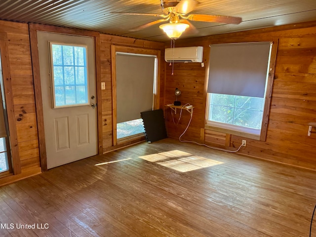 foyer with a wall unit AC, wooden walls, ceiling fan, and light hardwood / wood-style floors