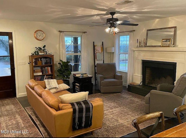 living area with visible vents, a fireplace with raised hearth, and a ceiling fan