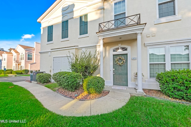 entrance to property with a balcony, a lawn, and central AC unit