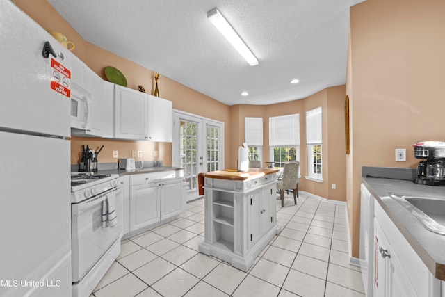 kitchen featuring white appliances, a center island, white cabinetry, and light tile patterned floors