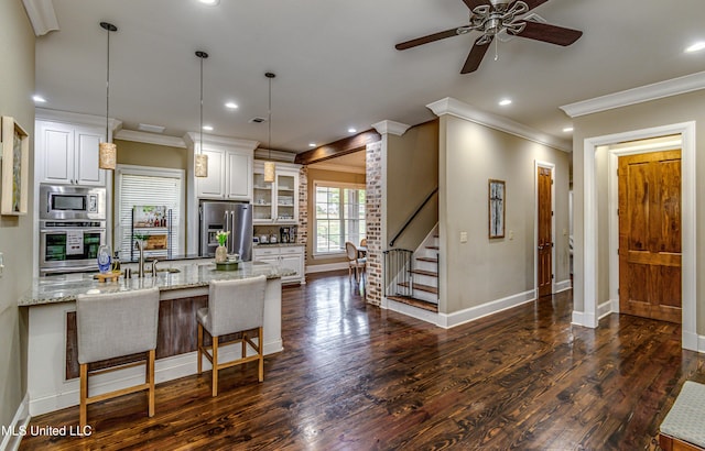 kitchen with light stone countertops, hanging light fixtures, stainless steel appliances, a breakfast bar, and white cabinets