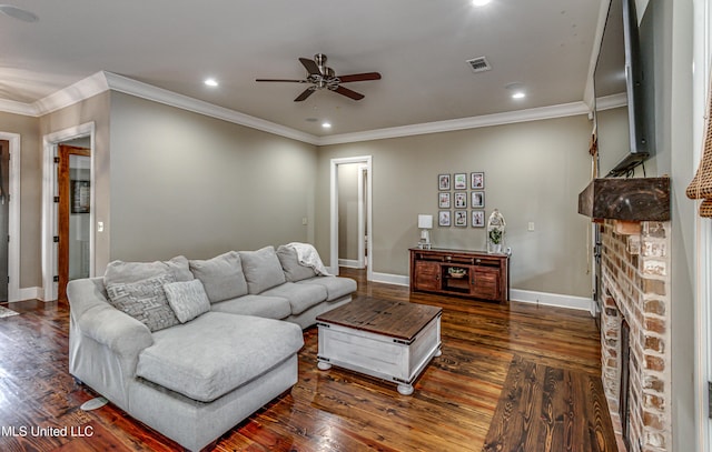 living room featuring crown molding, ceiling fan, dark wood-type flooring, and a stone fireplace