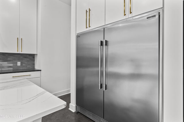 kitchen with built in fridge, white cabinets, and backsplash