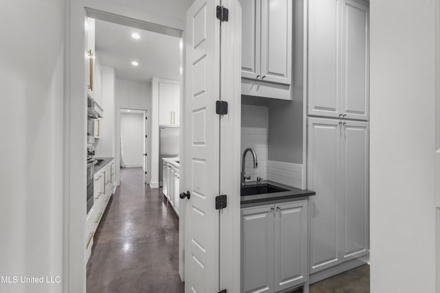 kitchen featuring recessed lighting, backsplash, white cabinets, a sink, and concrete flooring