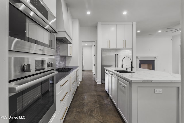 kitchen featuring stainless steel appliances, custom range hood, backsplash, an island with sink, and finished concrete floors