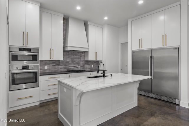 kitchen featuring a center island with sink, wall chimney exhaust hood, appliances with stainless steel finishes, finished concrete floors, and a sink