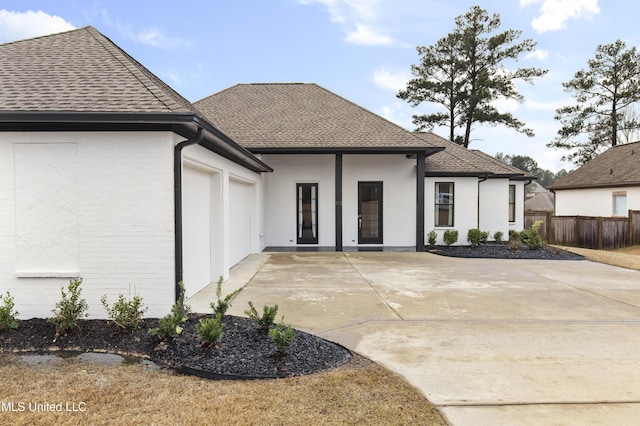 back of property featuring an attached garage, a shingled roof, fence, and concrete driveway