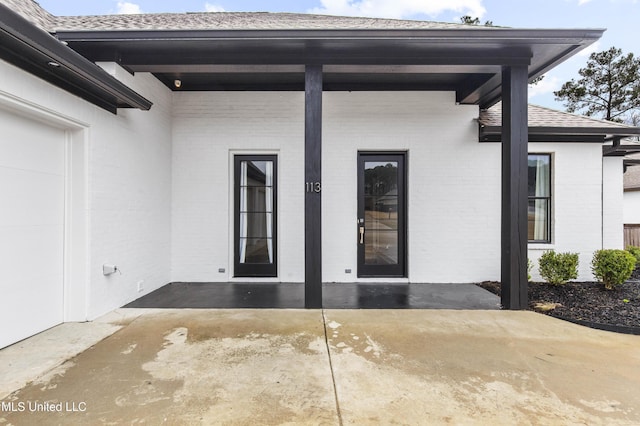 doorway to property featuring a patio area, brick siding, and a shingled roof